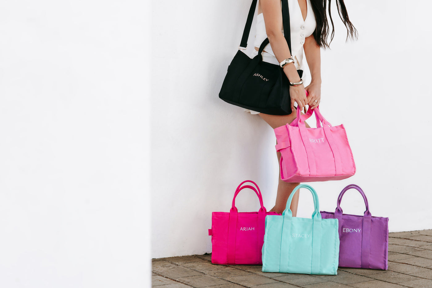 Woman holding a pink handbag with four other colorful bags on the ground.